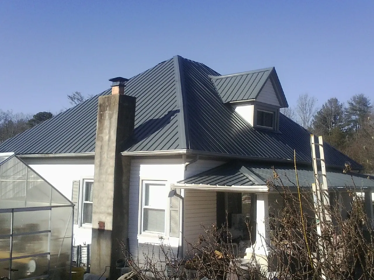 Dark blue standing seam metal roof on a white farmhouse with dormer — Slate & Tile Roof Repair by Roofing Brothers in Harrellsville