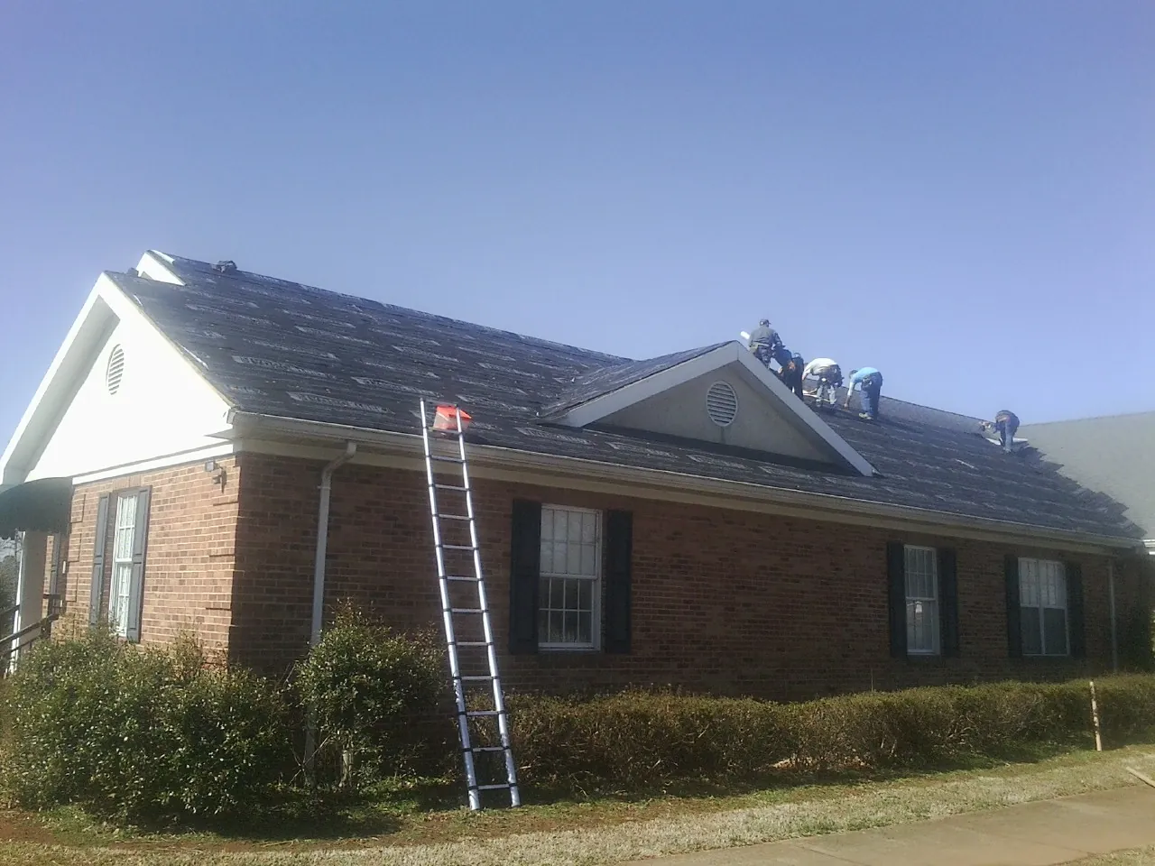 Crew tearing shingles off a brick ranch roof with a ladder set — Emergency Roof Repair work by our crew in Harrellsville
