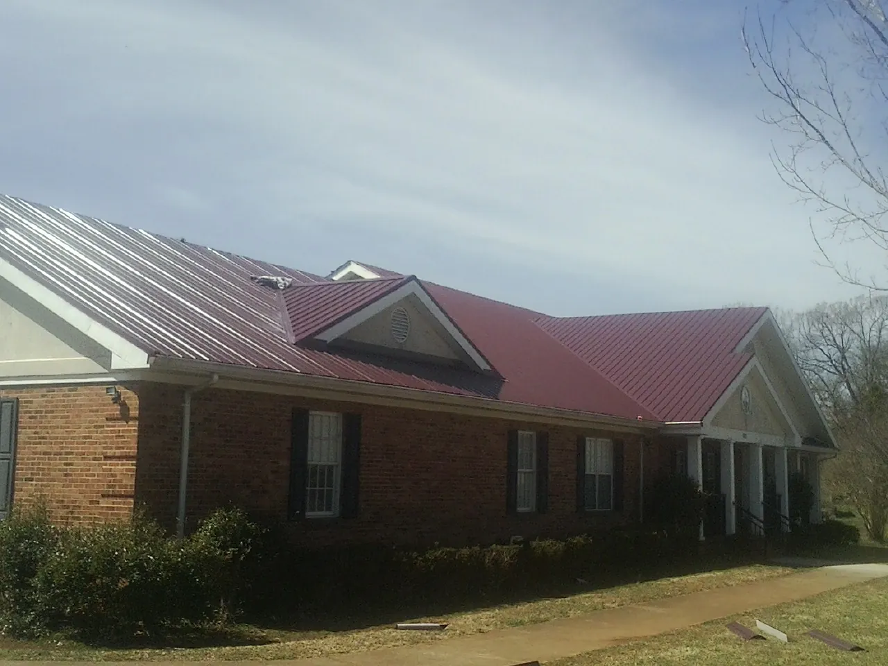 Red metal roof with gabled entries on a long brick building, from a Hail Damage Roof Repair job in Harrellsville