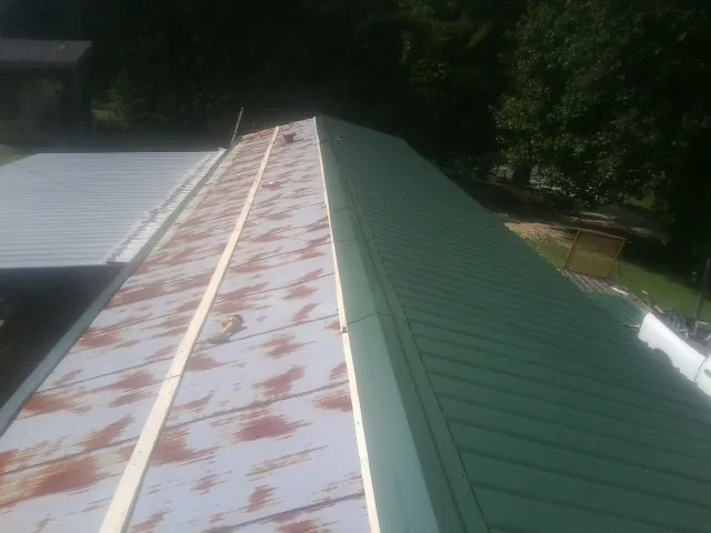 Old rusted panels beside newly installed green metal roofing — Wind Damage Roof Repair by Roofing Brothers in Harrellsville