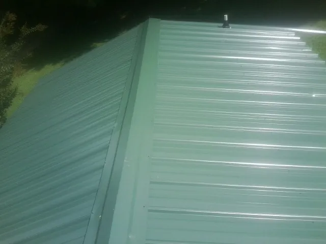 New green metal panels meeting at the ridge of a roof — Flat Roof Repair work by our crew in Harrellsville