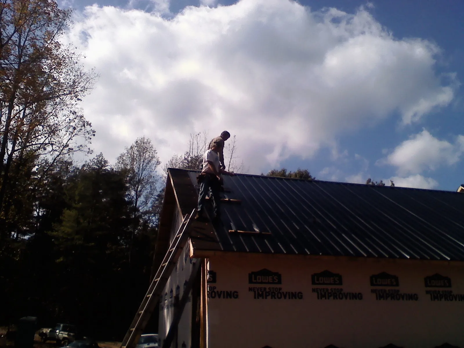 Roofer fastening dark metal panels high against a cloudy sky, from a Roof Inspection job in Harrellsville