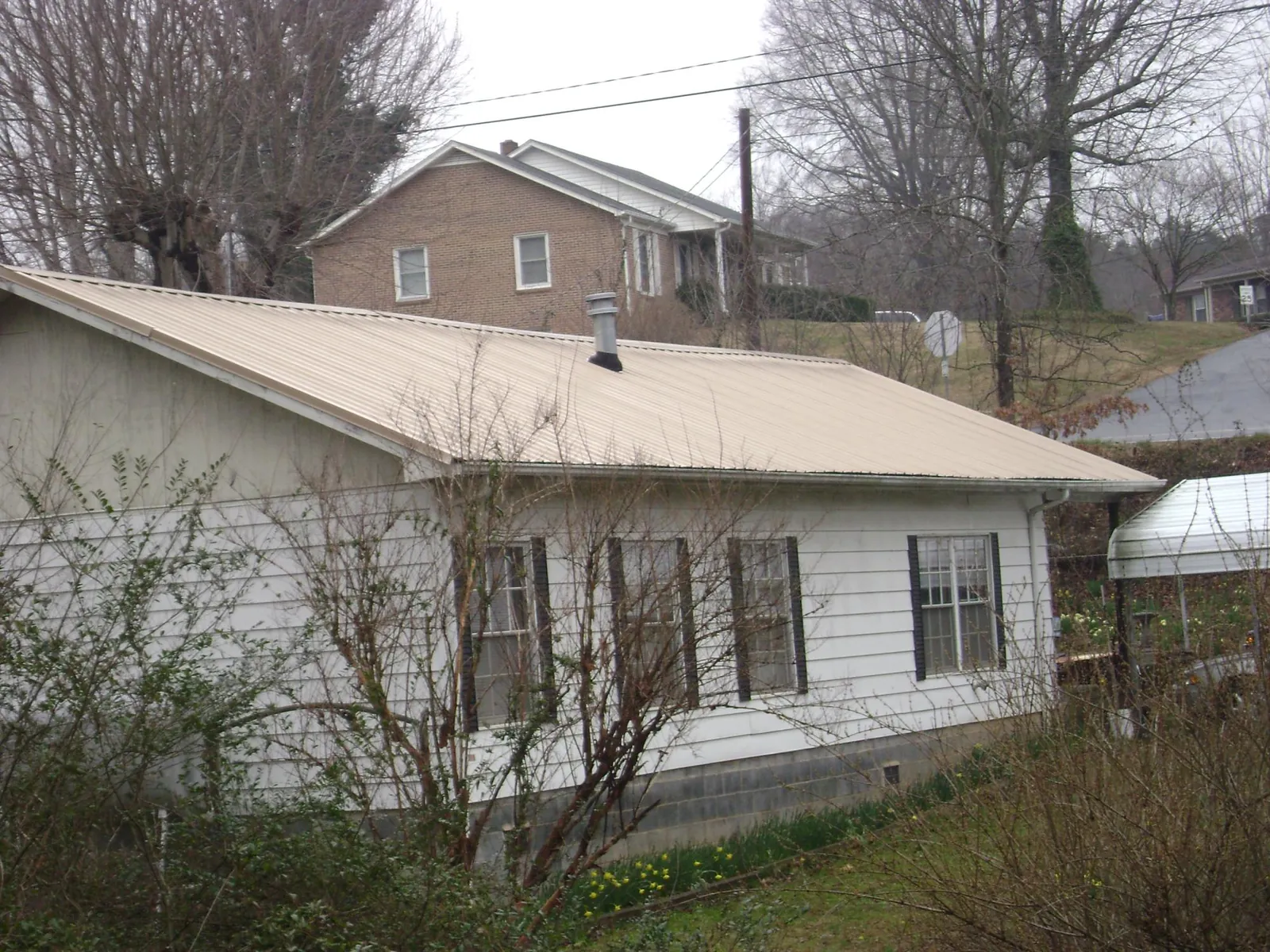 Tan metal roof on a white sided house set into a hillside — Commercial Roofing by Roofing Brothers in Harrellsville